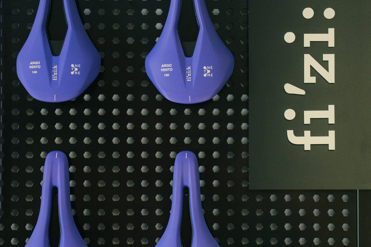 Four purple bike saddles on a black pegboard with 'fi'zi:k' branding. fizik one to one custom cycling saddles.